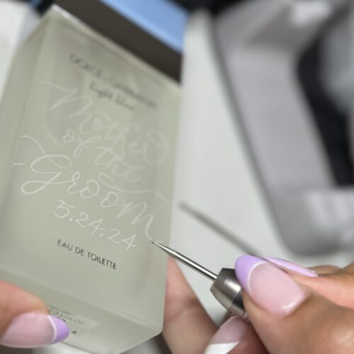 KeeKee.Creates artist hand-engraving a personalized name and wedding date on a luxury frosted glass perfume bottle, showcasing custom engraving services in Southern California