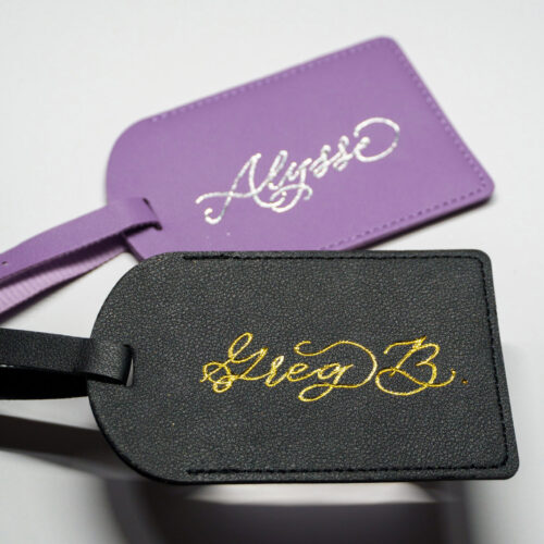 Custom leather luggage tags by KeeKee Creates featuring gold foil calligraphy names 'Alysse' and 'Greg B.' on purple and black tags